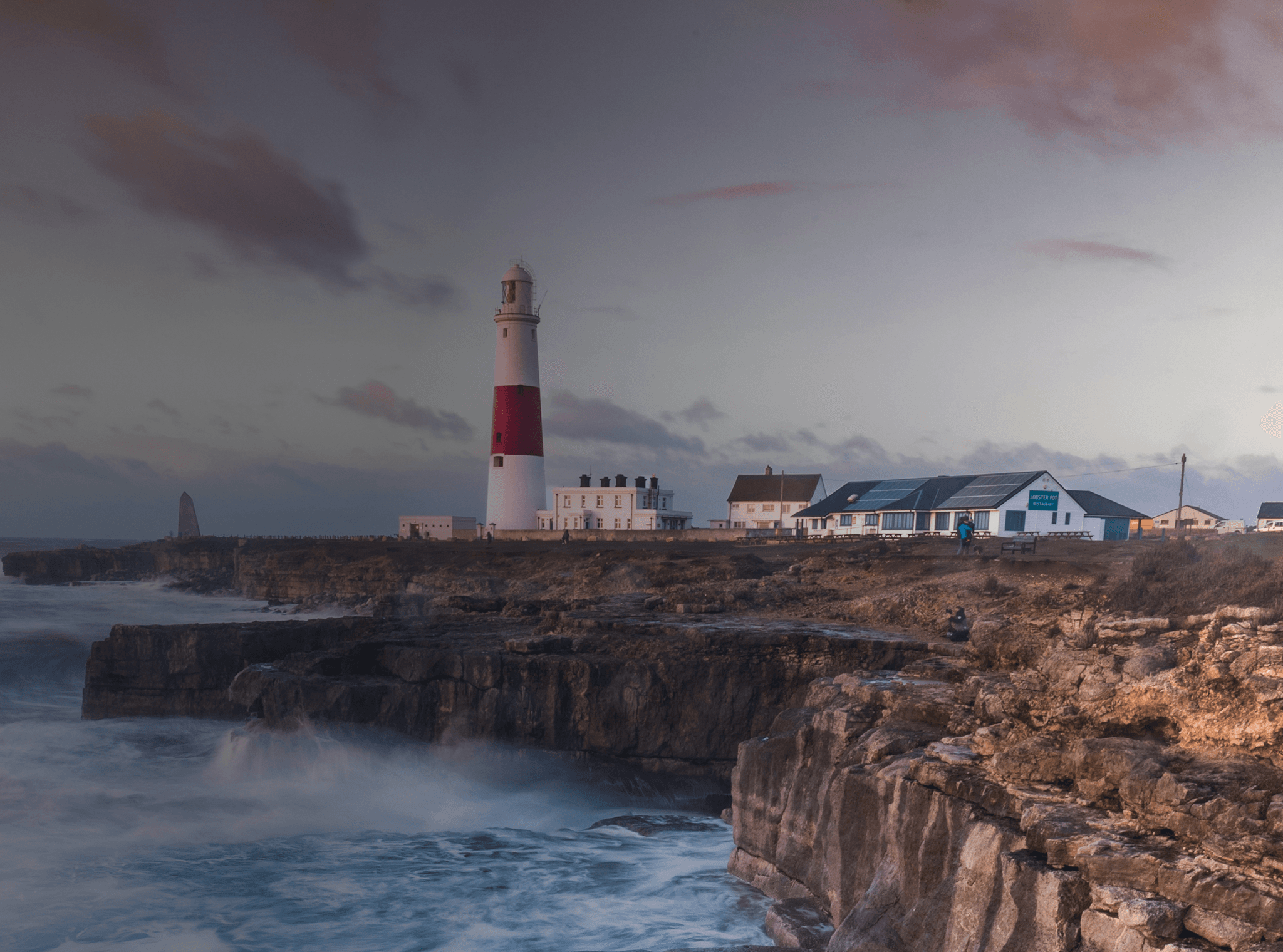 Le onde si infrangono su una scogliera britannica con un faro in lontananza