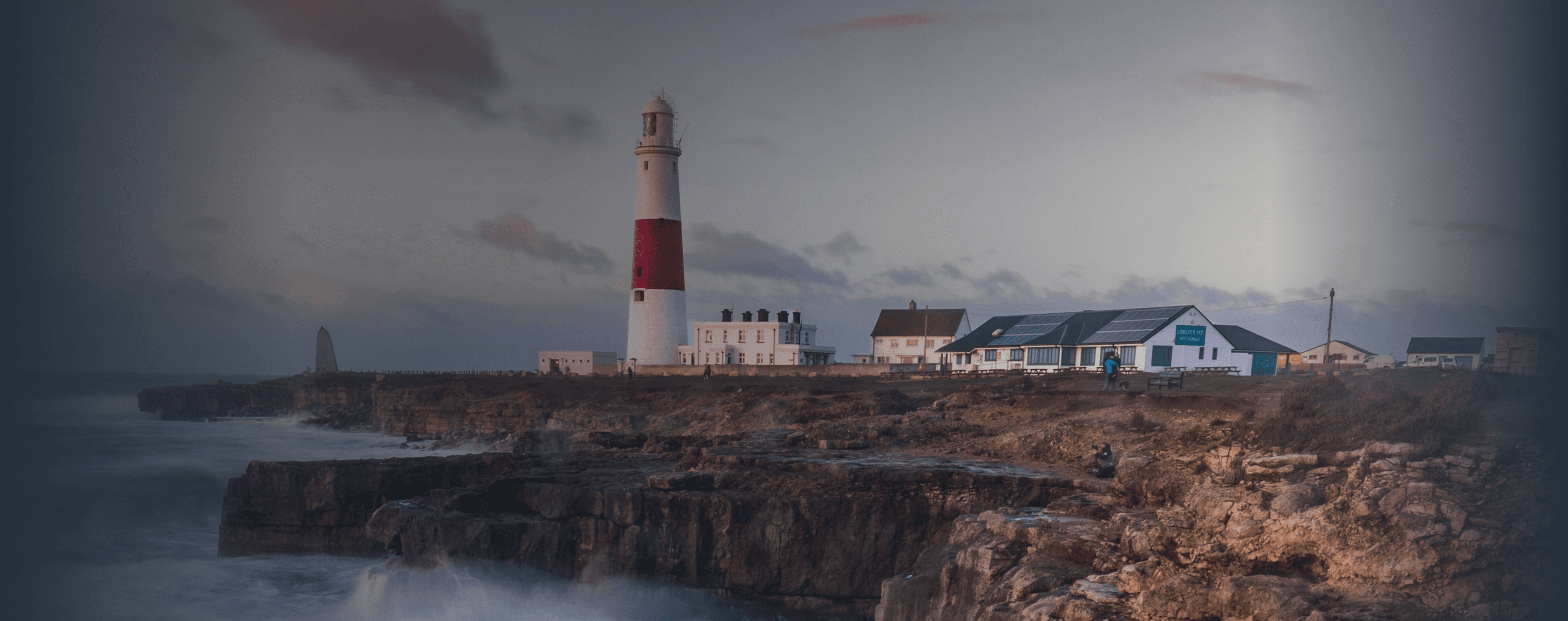 Le onde si infrangono su una scogliera britannica con un faro in lontananza