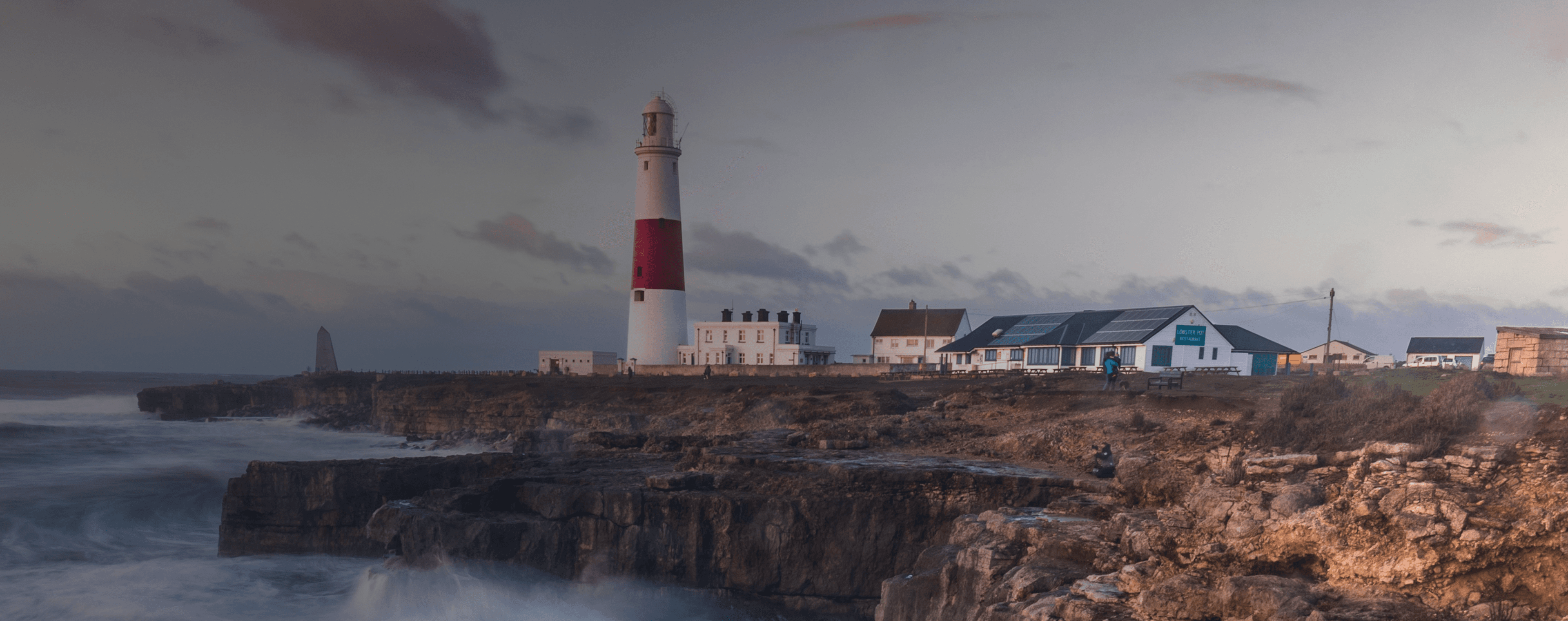 Le onde si infrangono su una scogliera britannica con un faro in lontananza