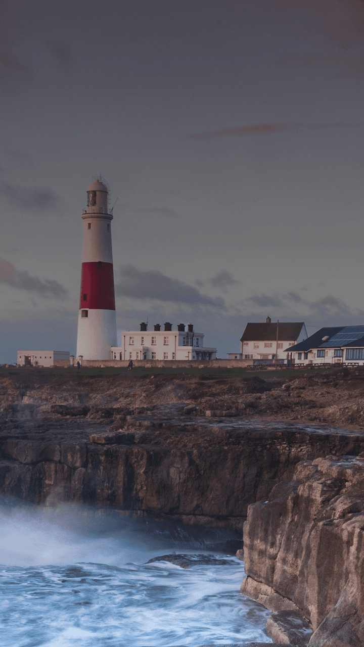 Le onde si infrangono su una scogliera britannica con un faro in lontananza