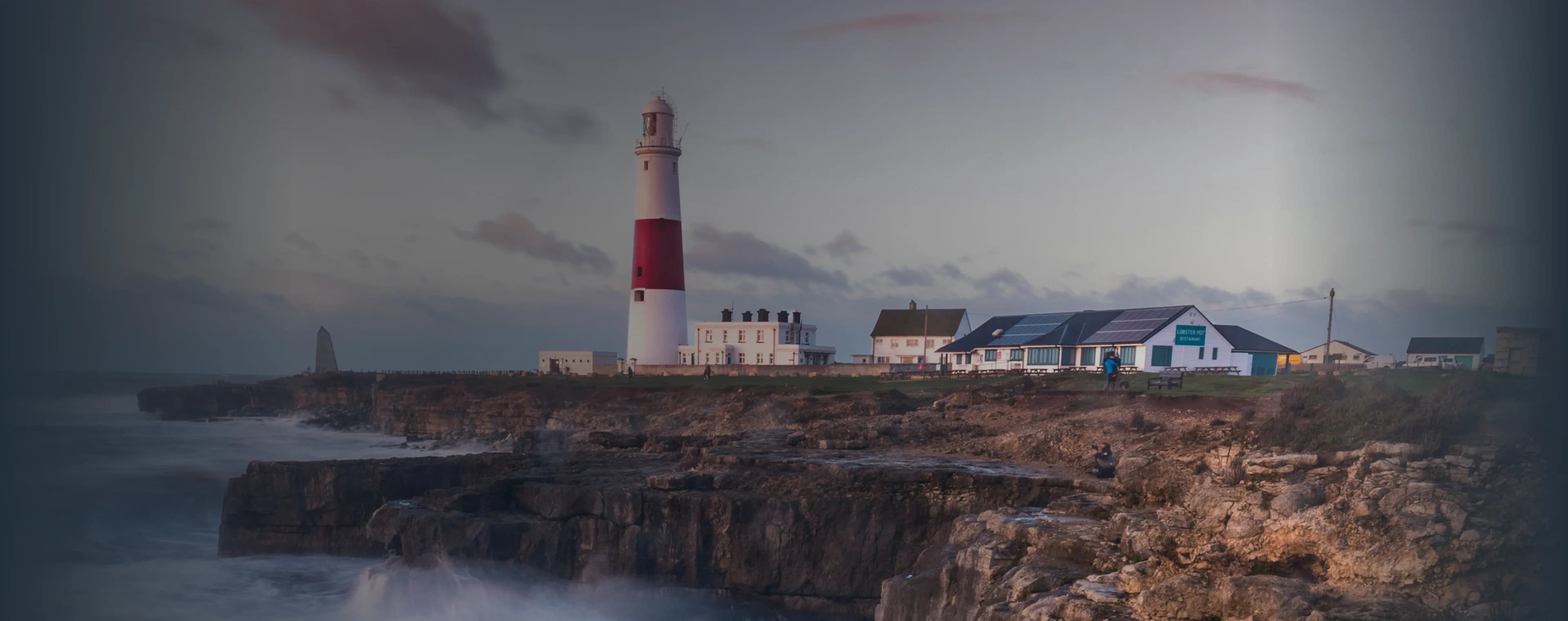 Le onde si infrangono su una scogliera britannica con un faro in lontananza