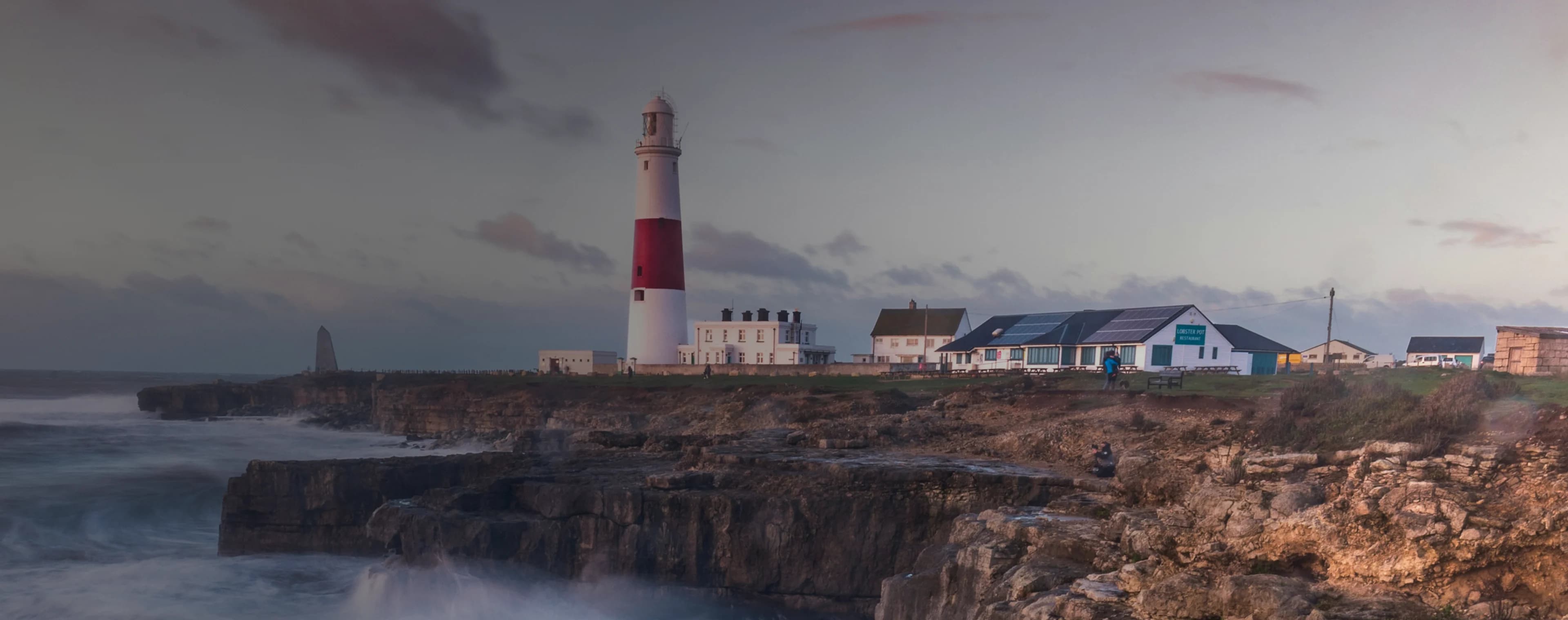 Le onde si infrangono su una scogliera britannica con un faro in lontananza